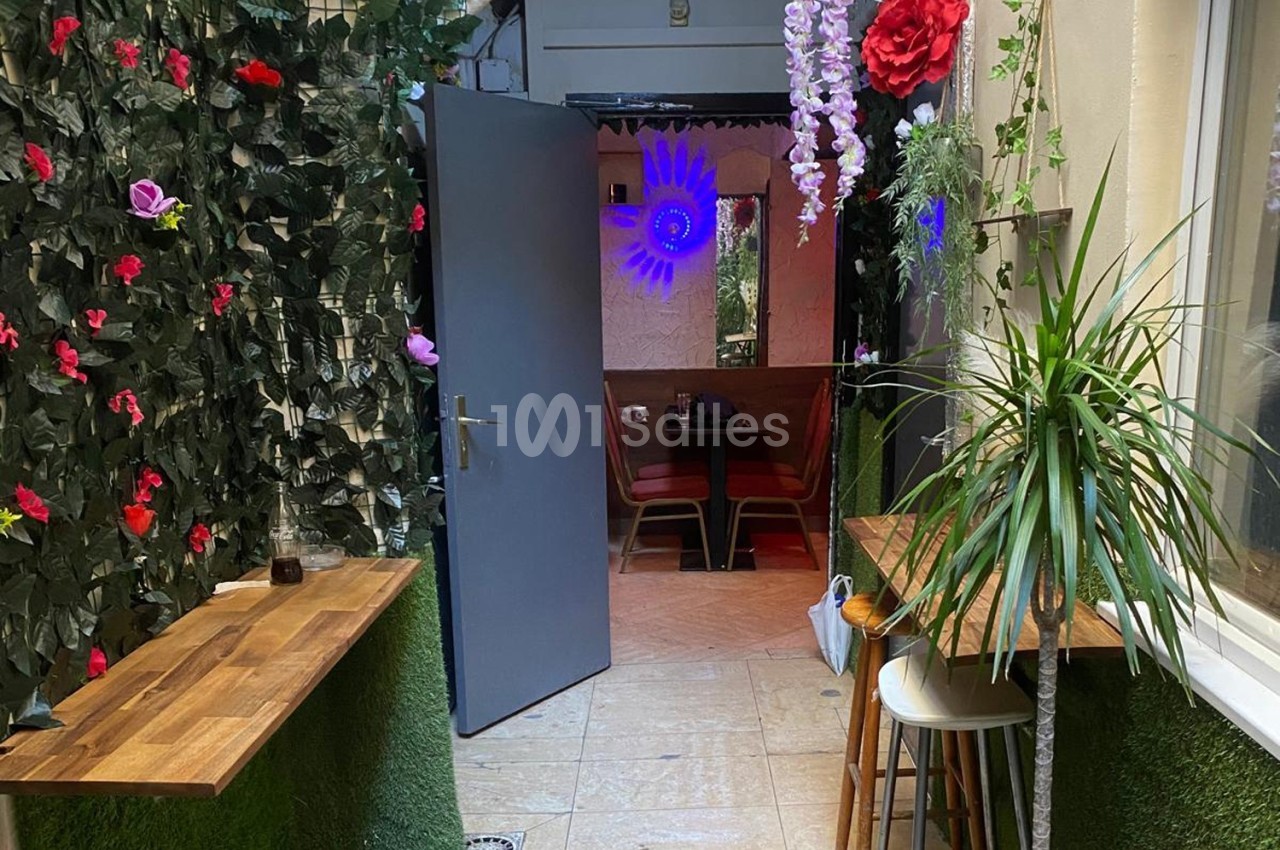 Entrée d'un espace intérieur avec plantes décoratives, tables en bois et lumière colorée en arrière-plan.