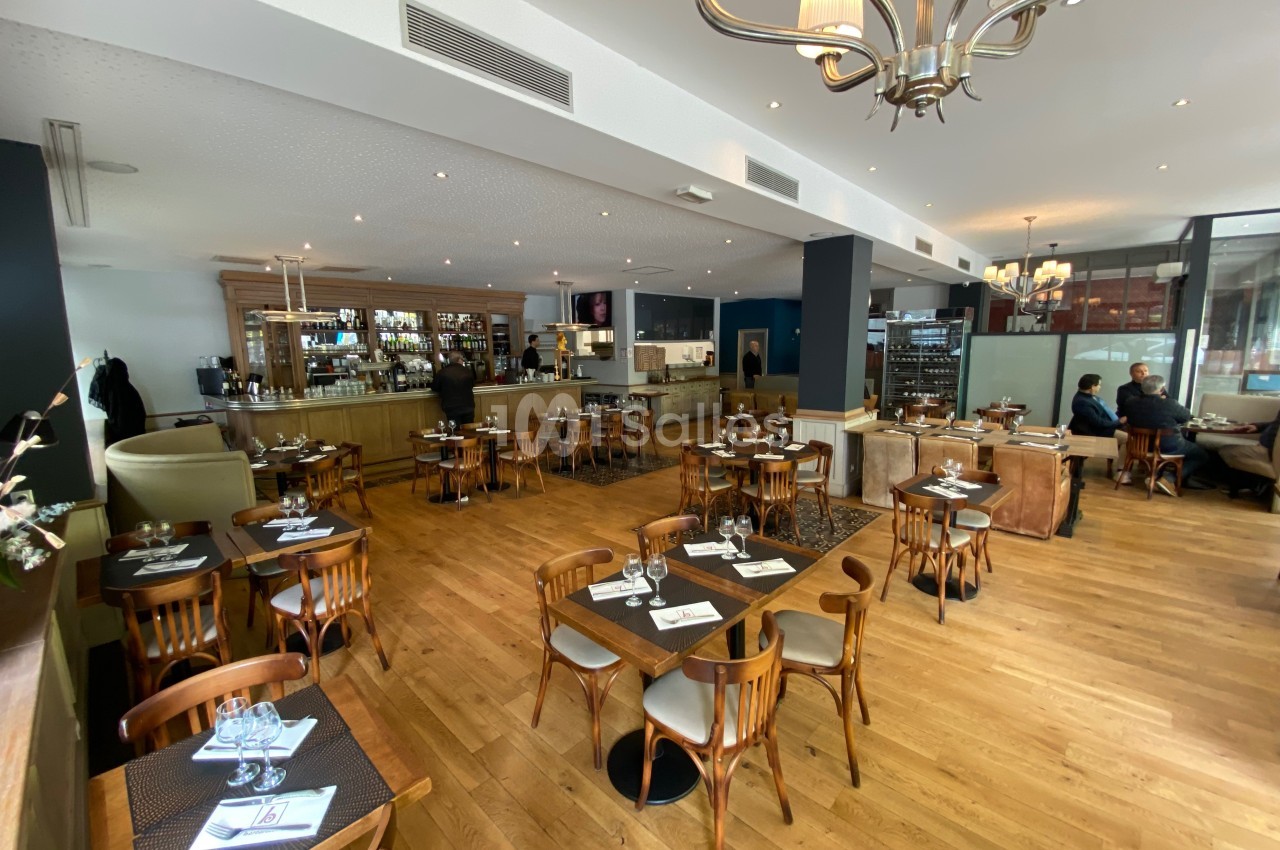 Salle de restaurant lumineuse avec tables en bois, chaises assorties et un bar en arrière-plan.