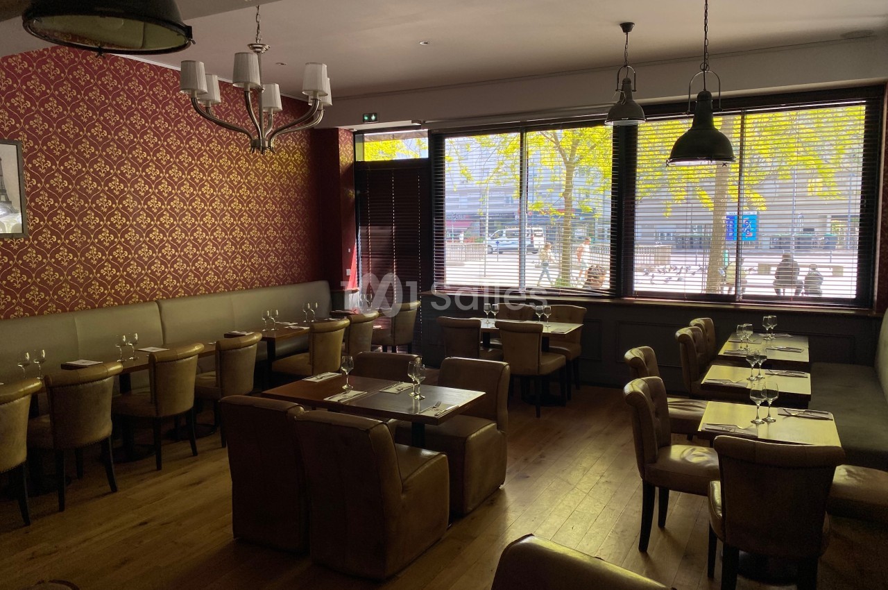 Salle de restaurant vide avec tables dressées, éclairée par la lumière naturelle entrant par de grandes fenêtres avec stores.