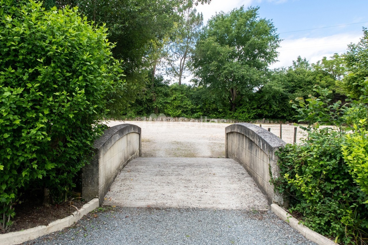 Petit pont en pierre traversant un chemin gravillonné, entouré de verdure et d'arbustes.