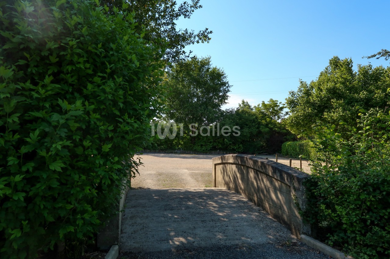 Petit pont en pierre menant à une allée entourée de verdure sous un ciel bleu clair.