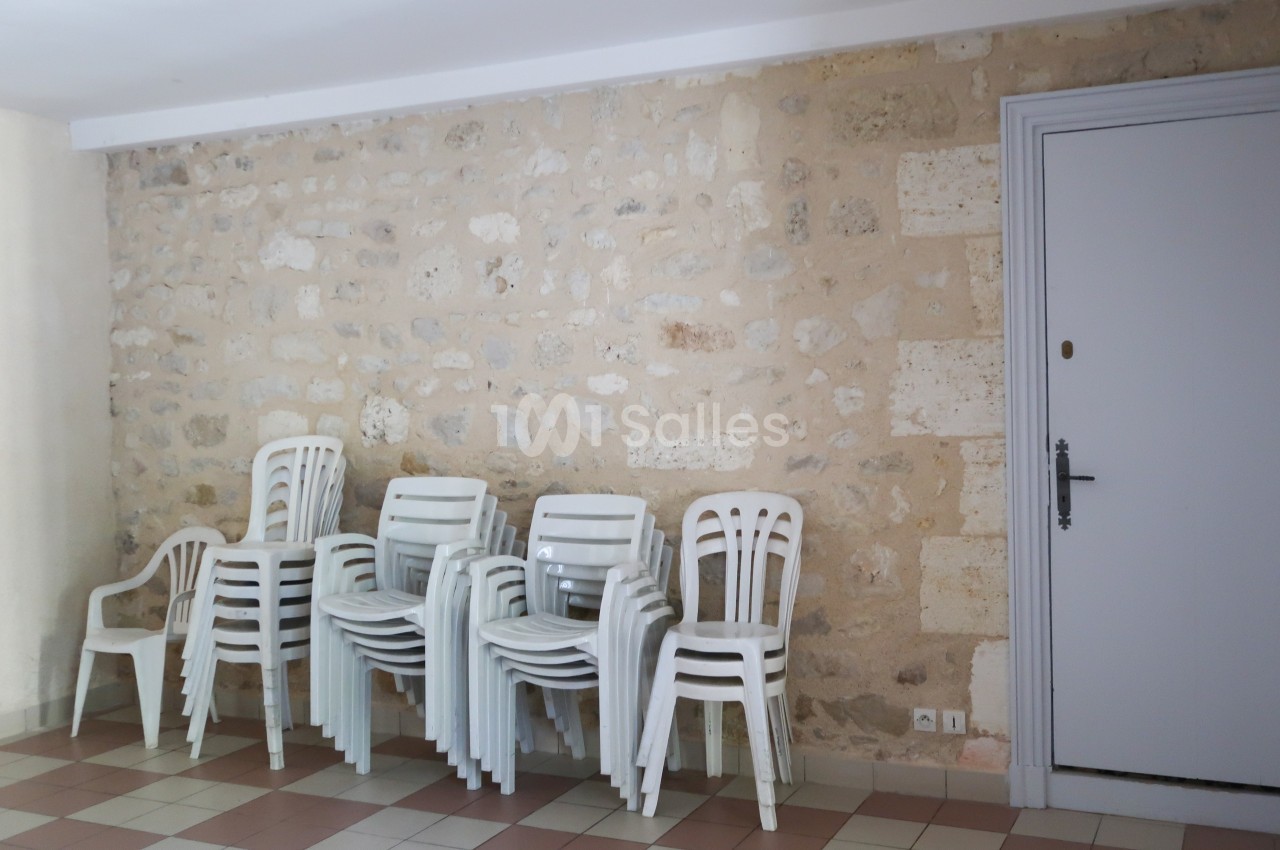Chaises en plastique blanc empilées dans une pièce avec un mur en pierre et un sol carrelé.