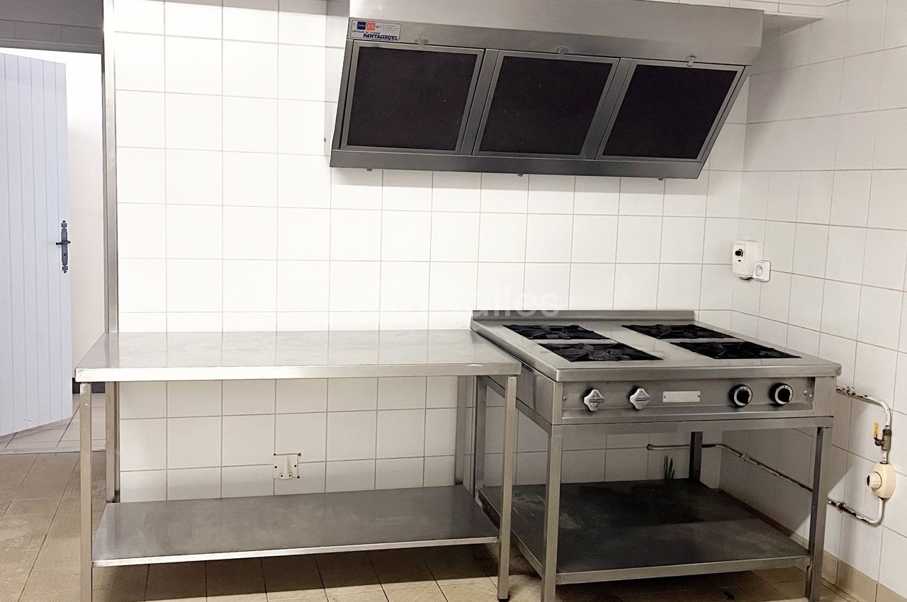 Cuisine professionnelle avec plan de travail en inox, plaque de cuisson à gaz et hotte d'extraction murale.