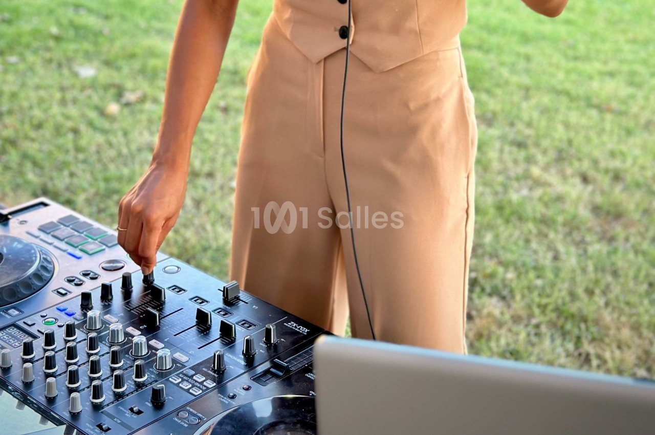 Personne ajustant les commandes d'une table de mixage en plein air, avec de l'herbe en arrière-plan.