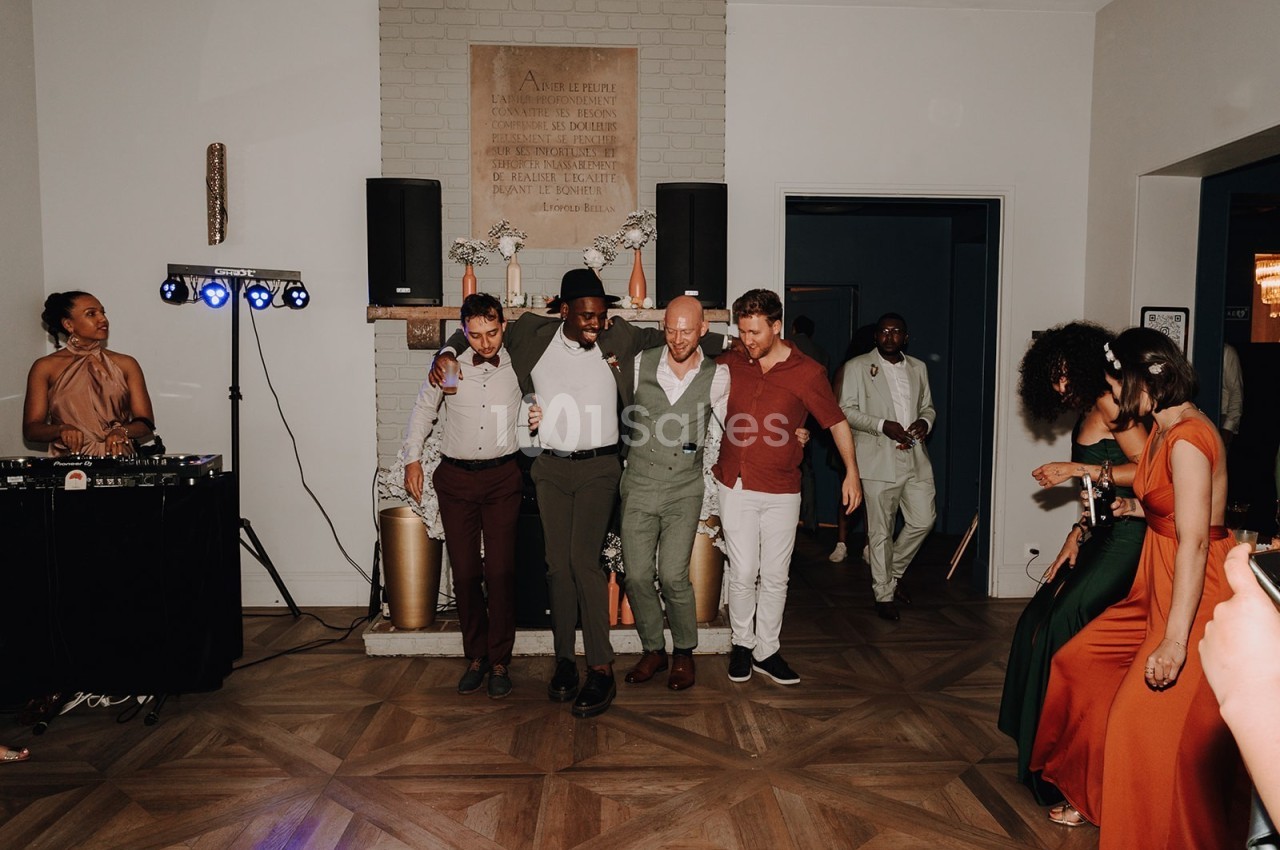 Des personnes dansent ensemble lors d'une fête, avec un DJ à gauche et des invités en arrière-plan.