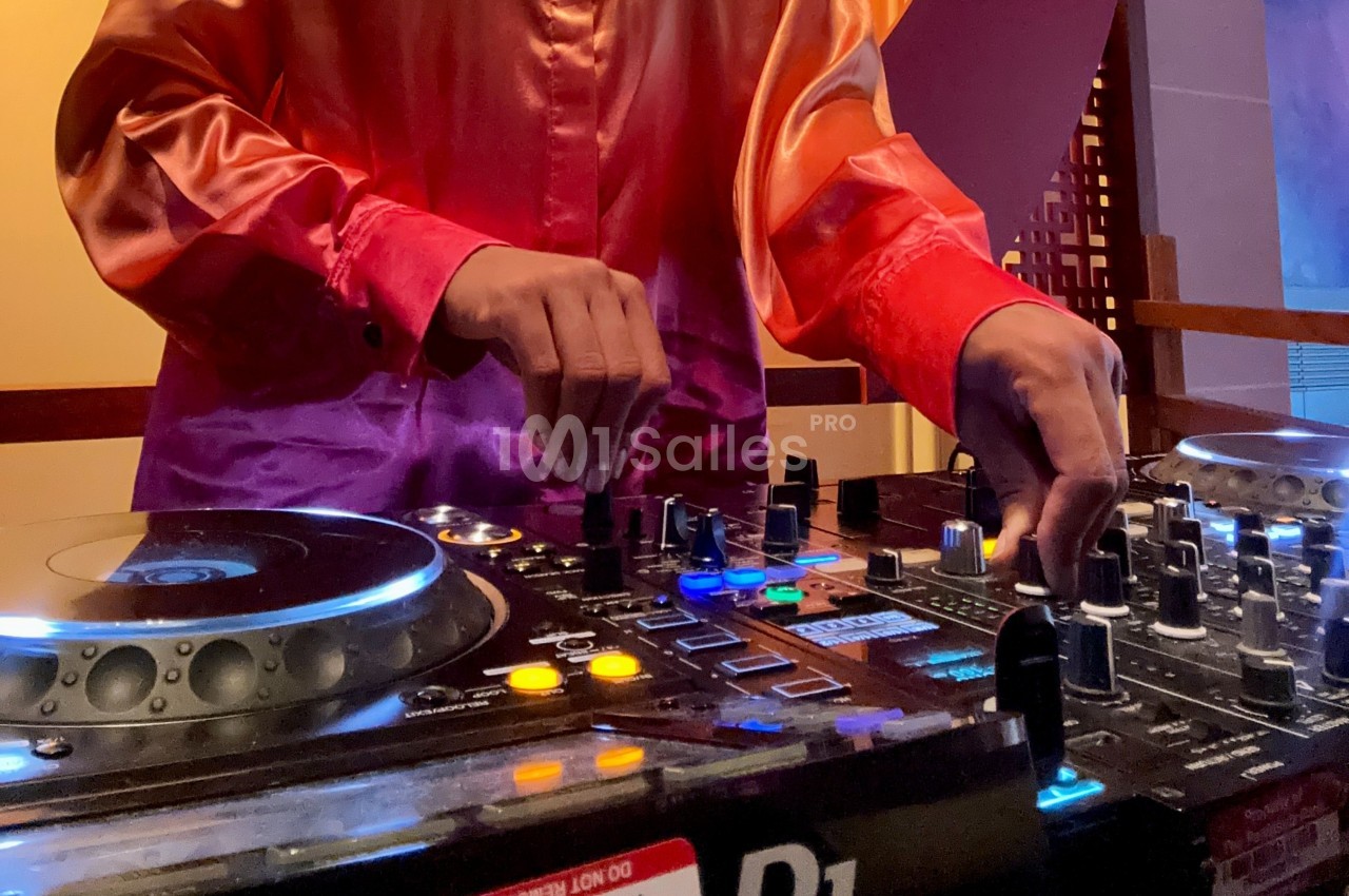 Personne utilisant une table de mixage avec des platines et des commandes lumineuses dans un environnement intérieur.