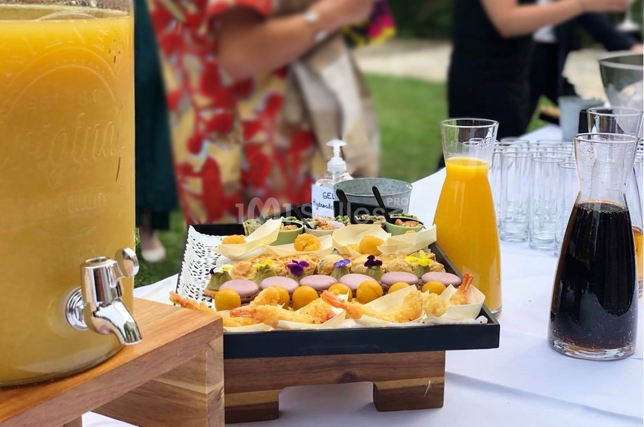 Buffet en extérieur avec jus de fruits, carafes et plateau de bouchées colorées décorées de fleurs comestibles.