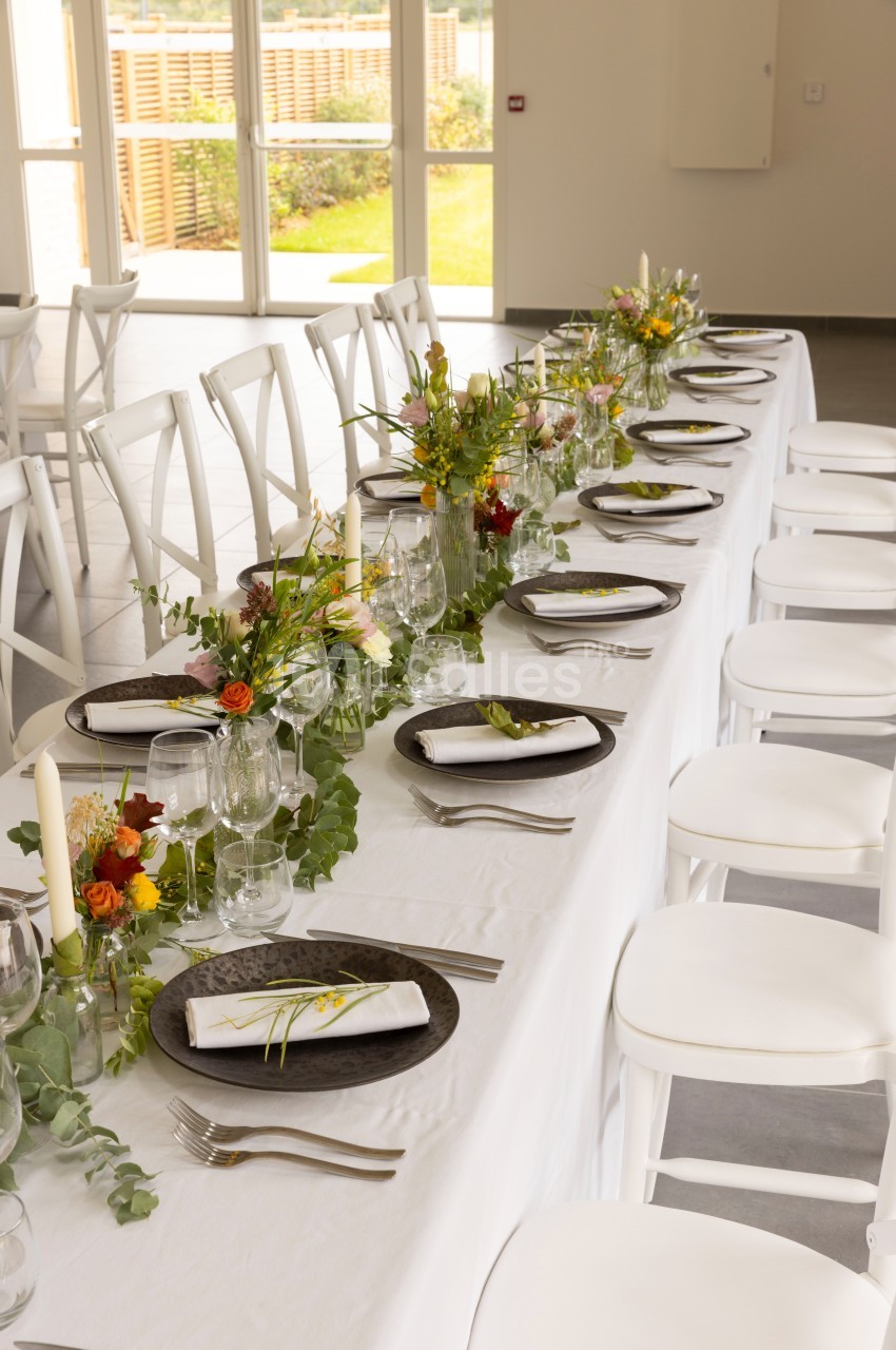 Table dressée avec une nappe blanche, vaisselle élégante, serviettes pliées et décorations florales colorées.