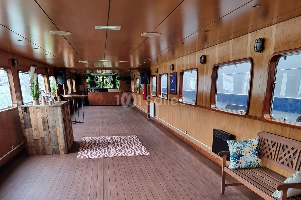 Intérieur d'une péniche aménagée avec un bar en bois, des fenêtres alignées et un espace de détente.