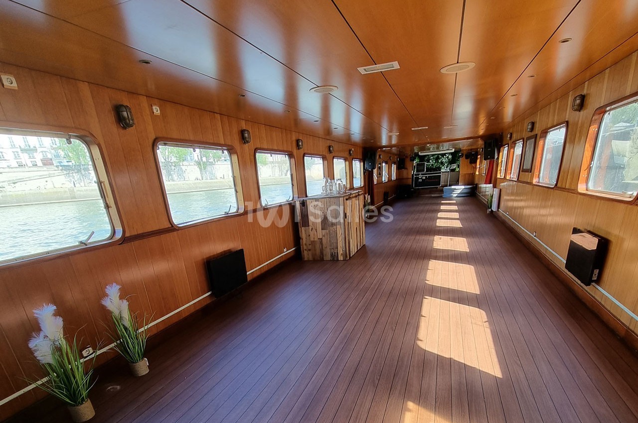 Intérieur d'une péniche avec parquet en bois, grandes fenêtres laissant entrer la lumière et quelques décorations simples.