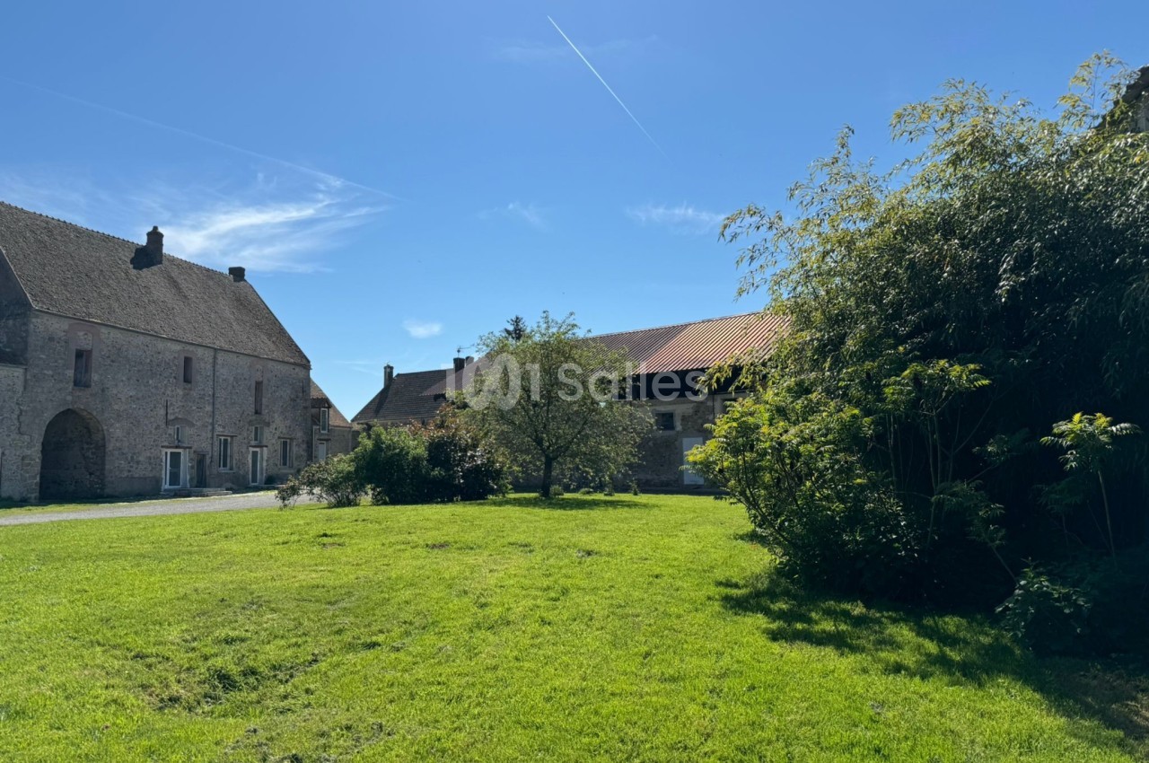 Cour verdoyante entourée de bâtiments en pierre et en bois sous un ciel bleu dégagé.