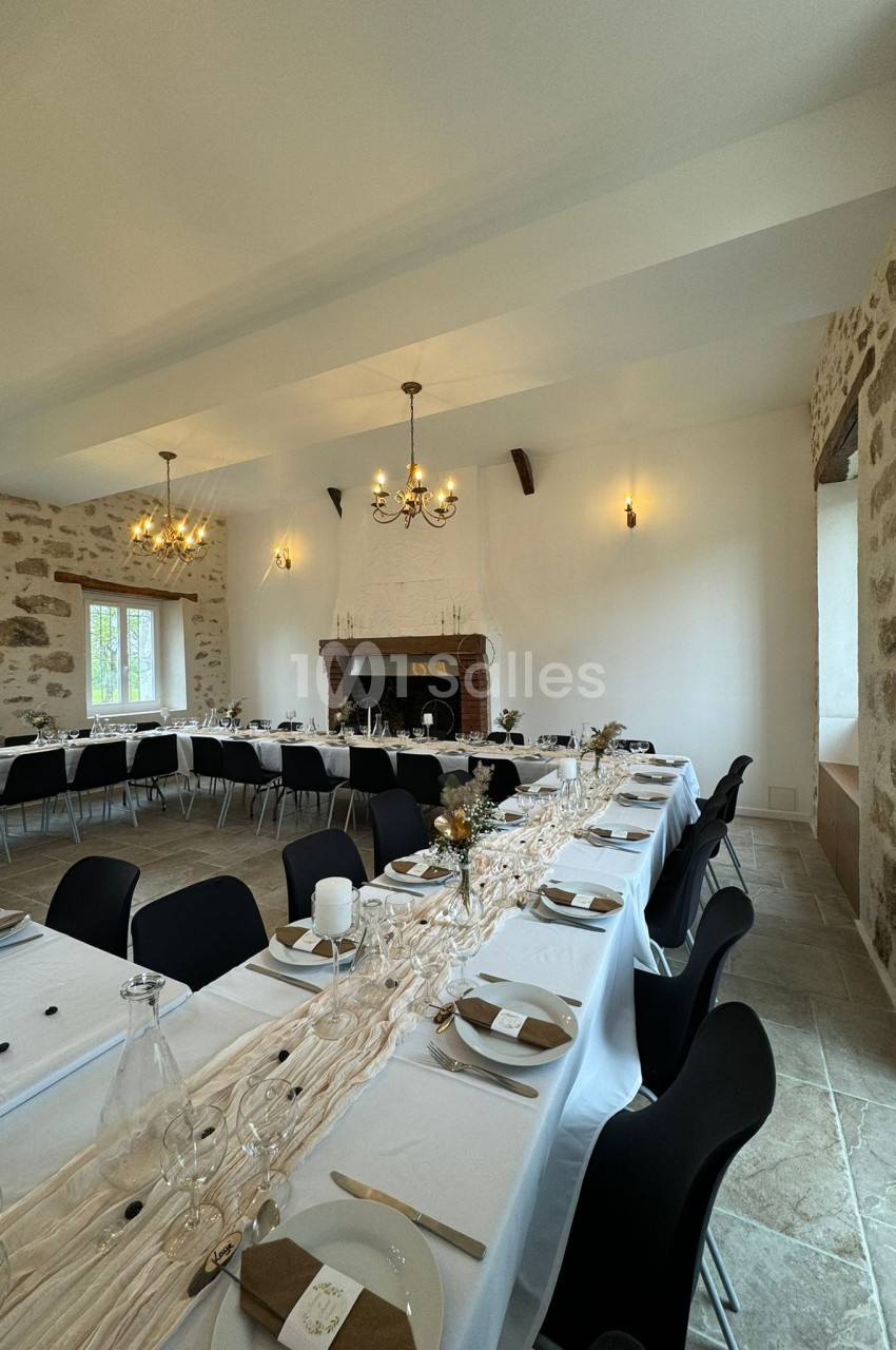 Salle de réception décorée avec des tables longues, nappes claires, vaisselle élégante et chandeliers suspendus.