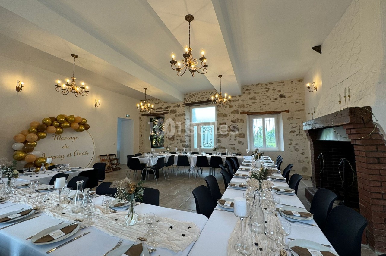 Salle de réception décorée pour un mariage, avec tables dressées, guirlande de ballons et cheminée en pierre.