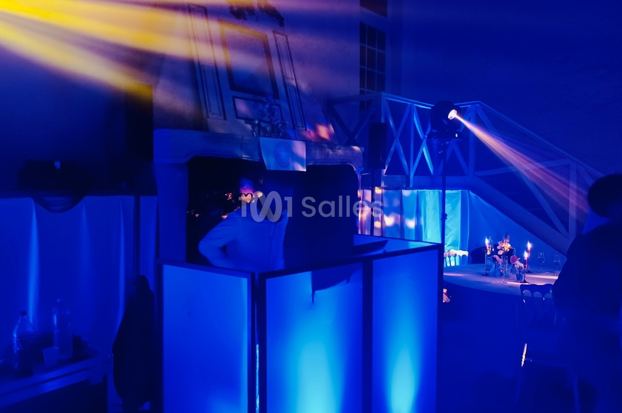 Une personne se tient derrière une console éclairée de lumières bleues dans une ambiance de soirée avec projecteurs colorés.
