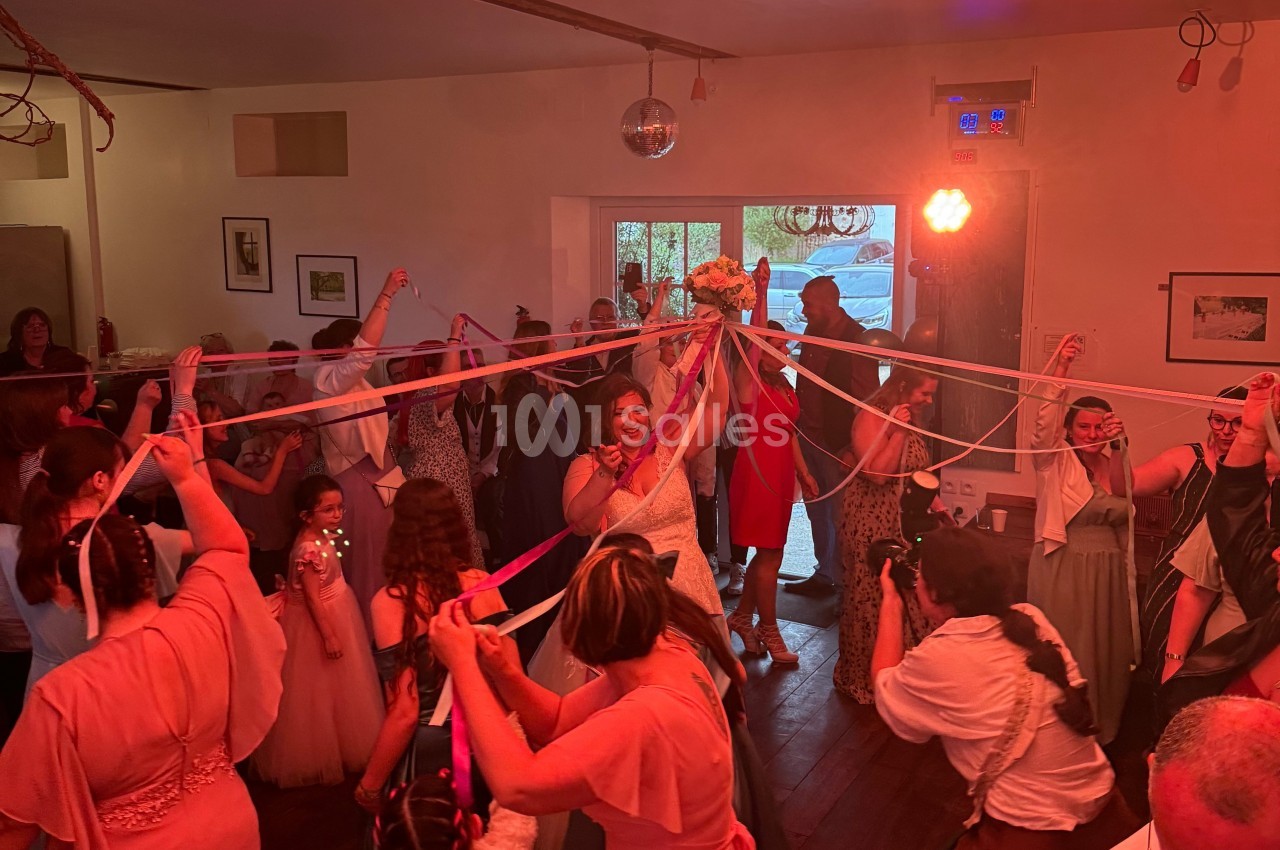 Des invités entourent une mariée avec des rubans colorés dans une salle décorée pour une fête.