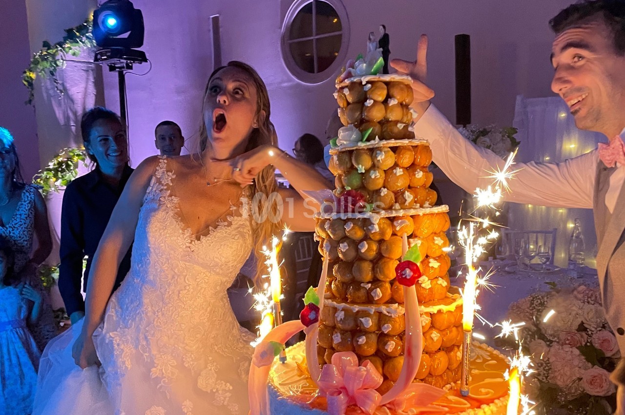 Une mariée surprise devant une pièce montée éclairée de bougies étincelantes lors d'une réception de mariage.