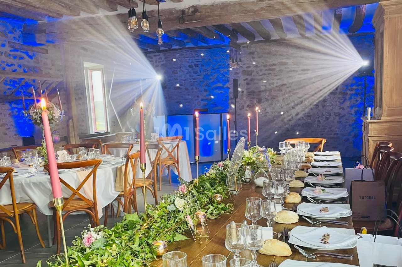 Salle de réception décorée pour un événement, avec tables dressées, bougies, guirlandes florales et éclairage tamisé.