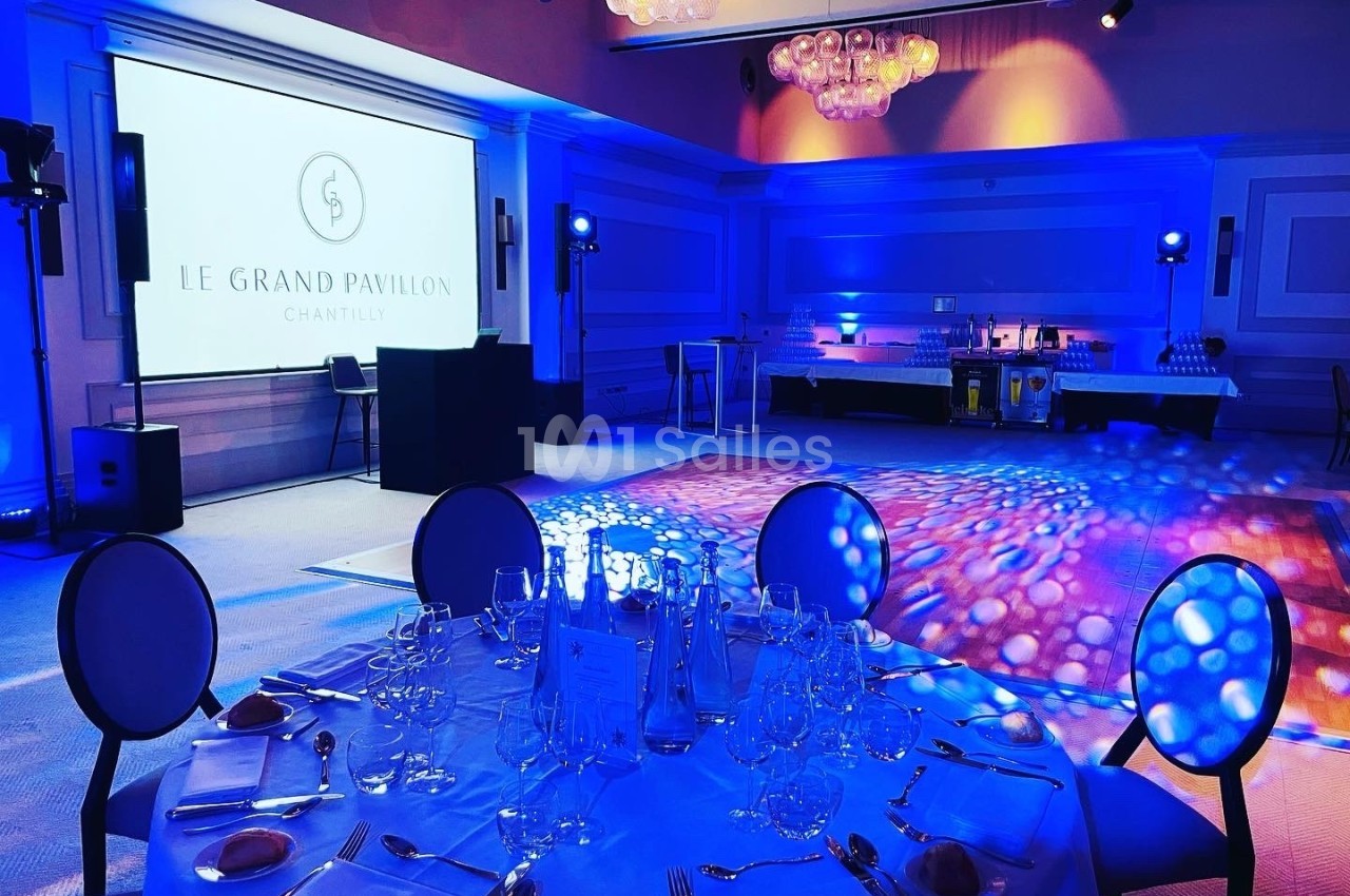 Salle de réception élégante avec table dressée au premier plan et piste de danse éclairée en arrière-plan.