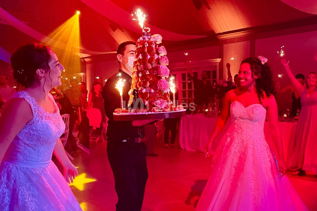 Un serveur apporte une pièce montée décorée de bougies étincelantes lors d'une réception de mariage animée.
