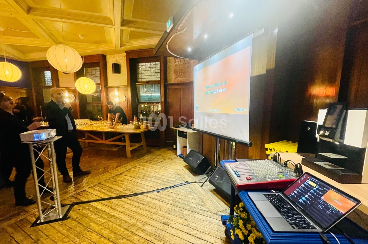 Salle avec parquet en bois, écran de projection, table de buffet éclairée et matériel audio visible au premier plan.