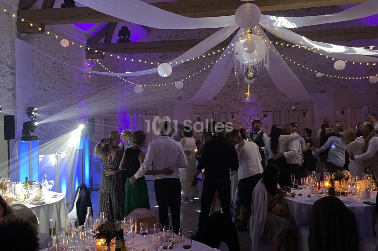 Salle de réception décorée avec des guirlandes lumineuses, des invités dansant et des tables dressées pour un événement.