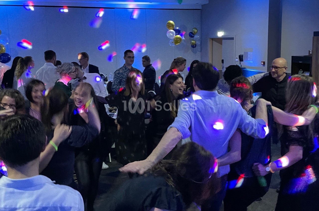 Groupe de personnes dansant dans une salle éclairée par des lumières colorées lors d'un événement festif.