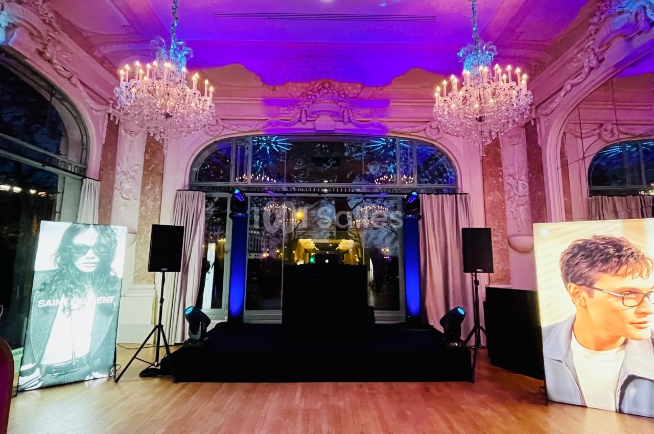 Salle élégante avec lustres, scène centrale éclairée et affiches de mannequins de chaque côté.