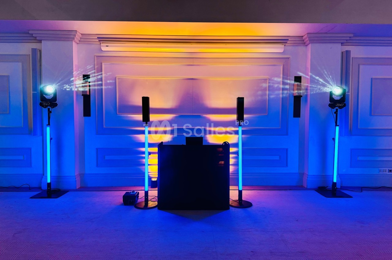 Installation lumineuse avec projecteurs colorés bleus et jaunes éclairant un mur blanc et un pupitre central.