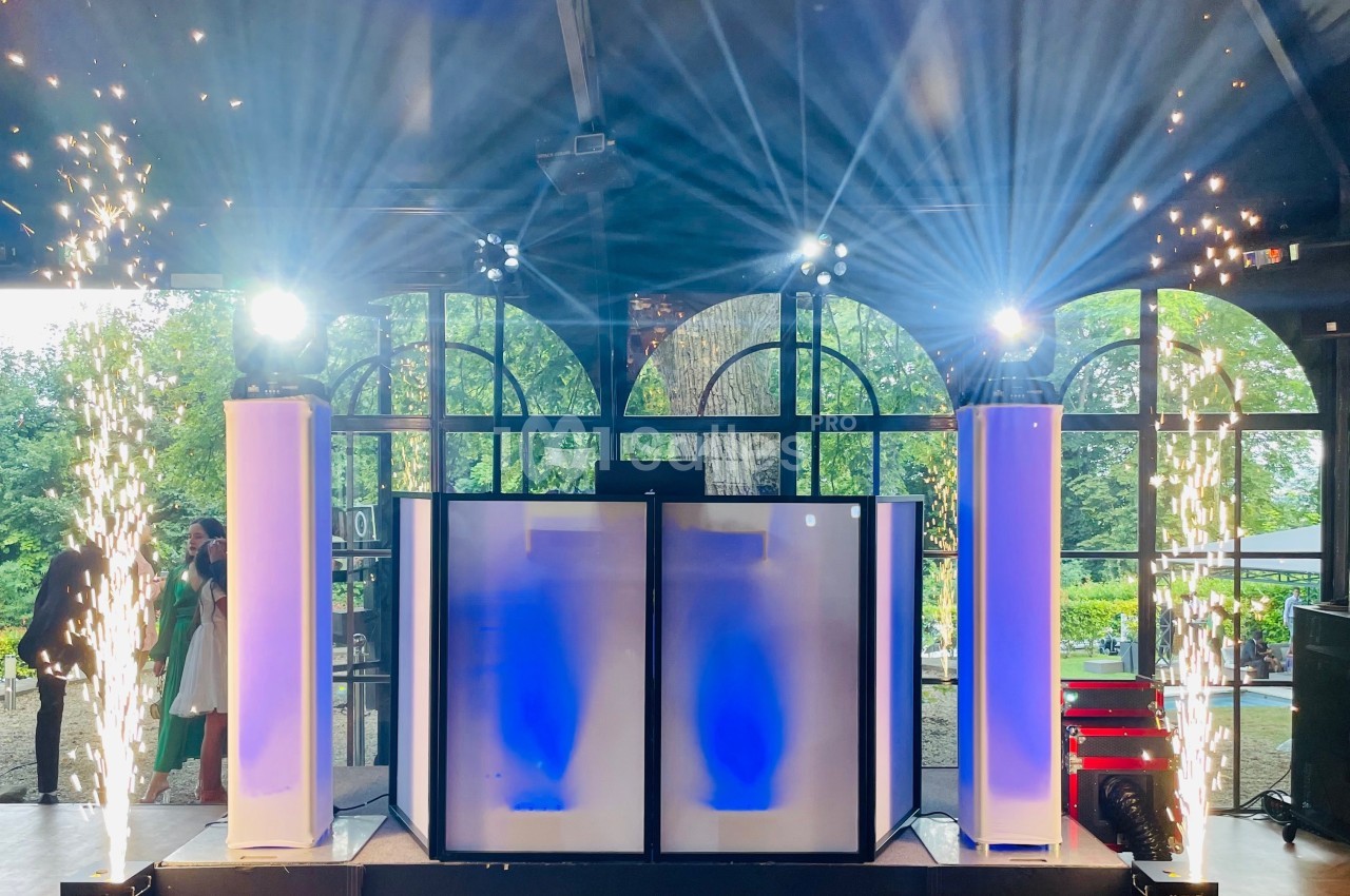 Poste de DJ éclairé avec des colonnes lumineuses, des effets pyrotechniques et une grande baie vitrée en arrière-plan.