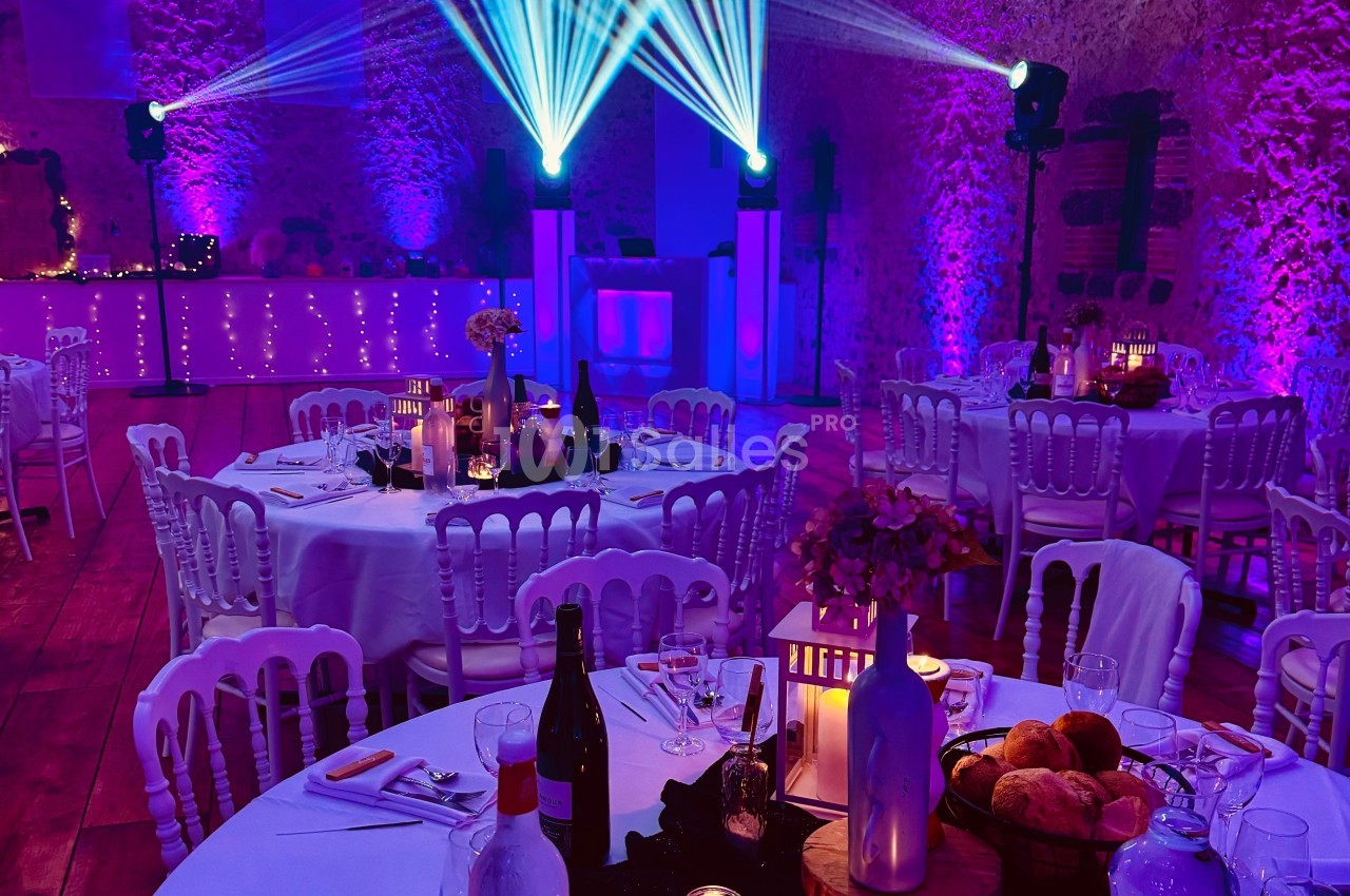 Salle de réception décorée avec des tables rondes, éclairages violets et projecteurs lumineux.