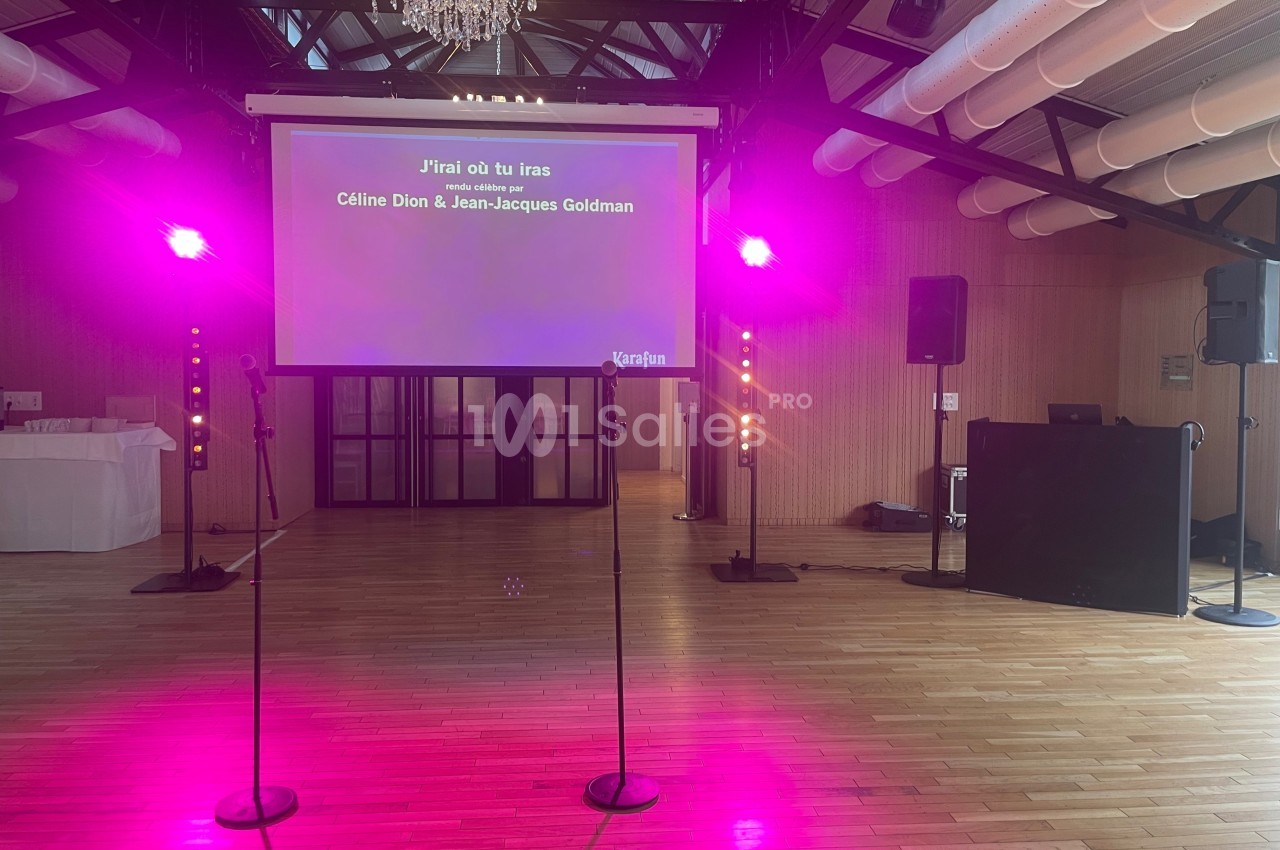 Écran de karaoké affichant les paroles de ’J'irai où tu iras’ dans une salle éclairée par des lumières roses.
