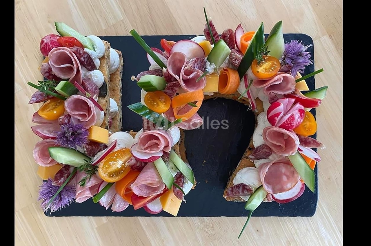 Plateau en forme de couronne garni de charcuterie, légumes frais, fromage et fleurs comestibles sur ardoise noire.