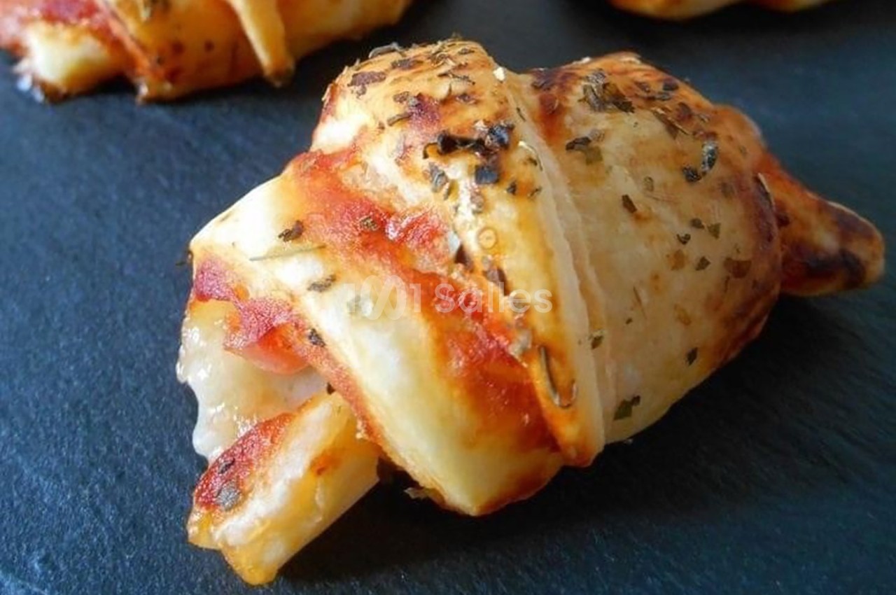Croissant apéritif doré garni de fromage fondant et de jambon, posé sur une surface en ardoise.