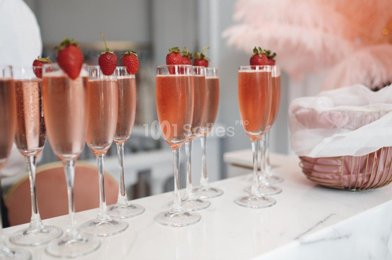 Verres de champagne rosé garnis de fraises fraîches alignés sur un comptoir blanc.