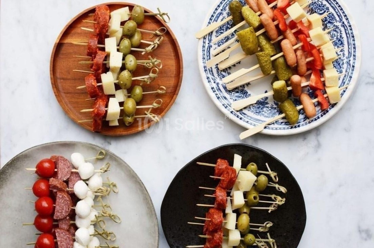 Assortiment de brochettes apéritives avec légumes, fromages, charcuteries et olives sur des assiettes variées.