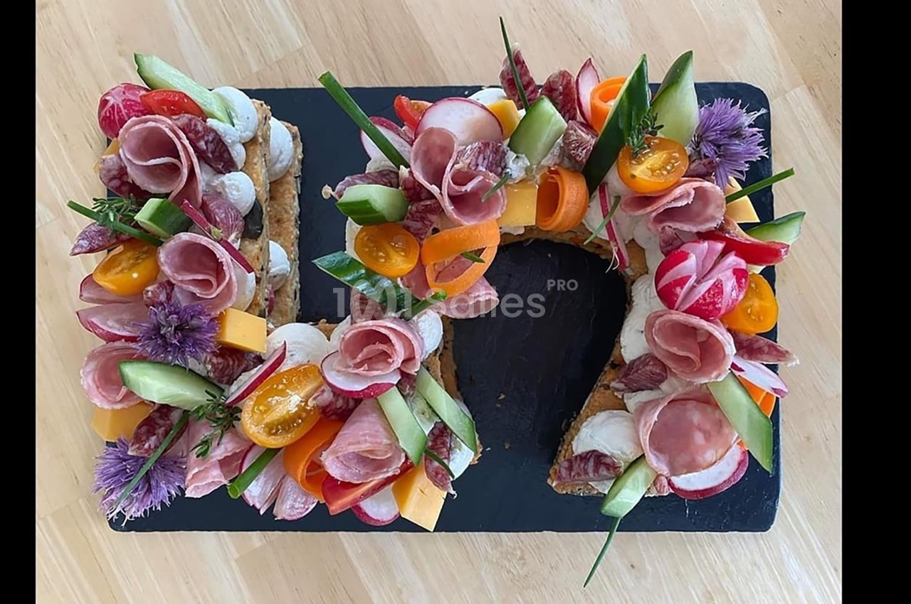 Plateau en forme de couronne garni de charcuterie, légumes frais, fromage et fleurs comestibles sur ardoise noire.