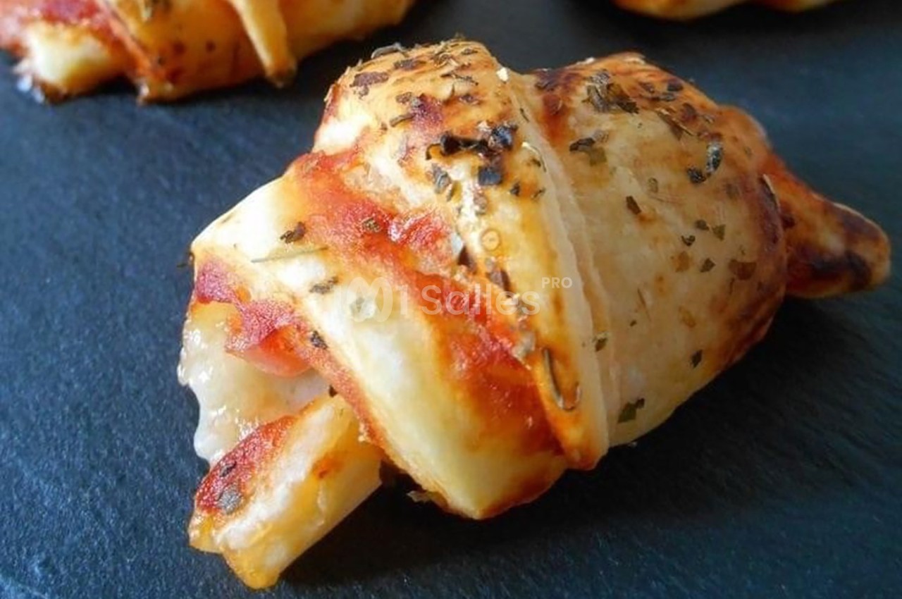 Croissant apéritif doré garni de fromage fondant et de jambon, posé sur une surface en ardoise.