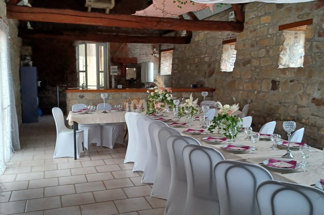 Salle de réception en pierre avec tables décorées de nappes blanches, fleurs et vaisselle pour un événement festif.