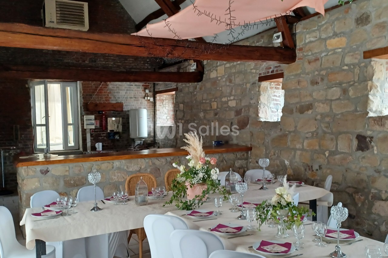 Salle en pierre avec une grande table dressée pour un repas, décorée de fleurs et de serviettes roses.