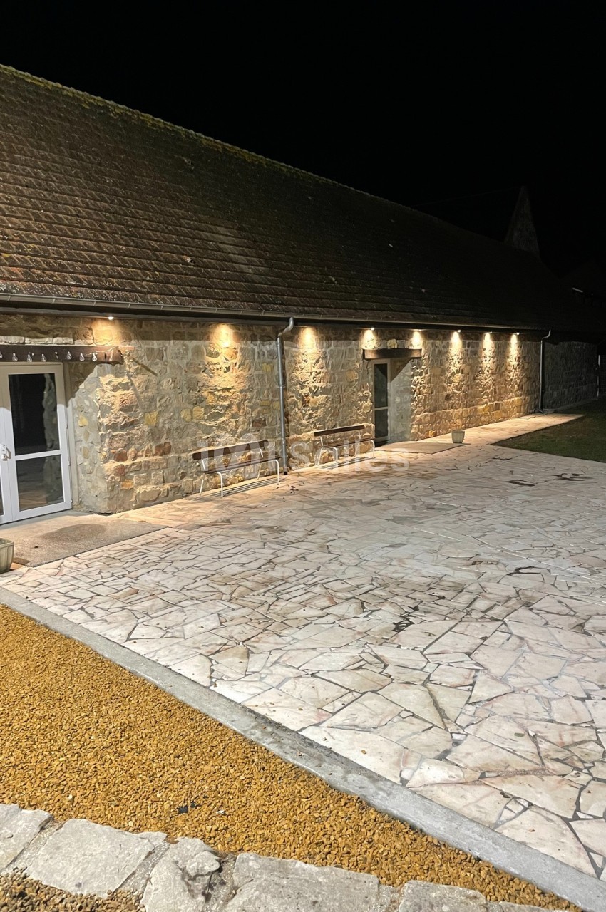 Cour en pierre éclairée la nuit, bordée par un bâtiment en pierre avec des lumières murales.