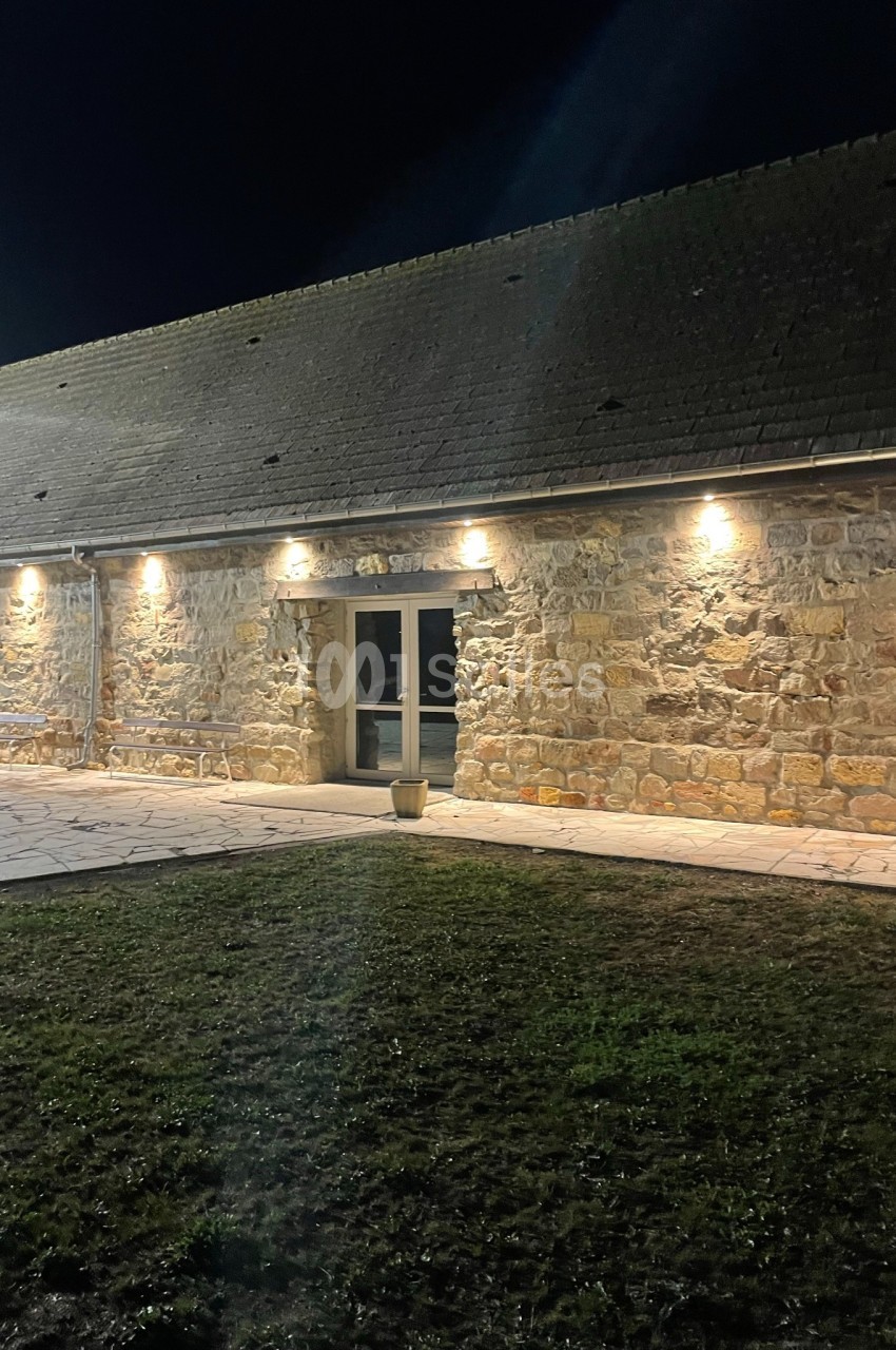 Façade en pierre d'un bâtiment éclairé par des appliques murales, avec une porte vitrée au centre, de nuit.
