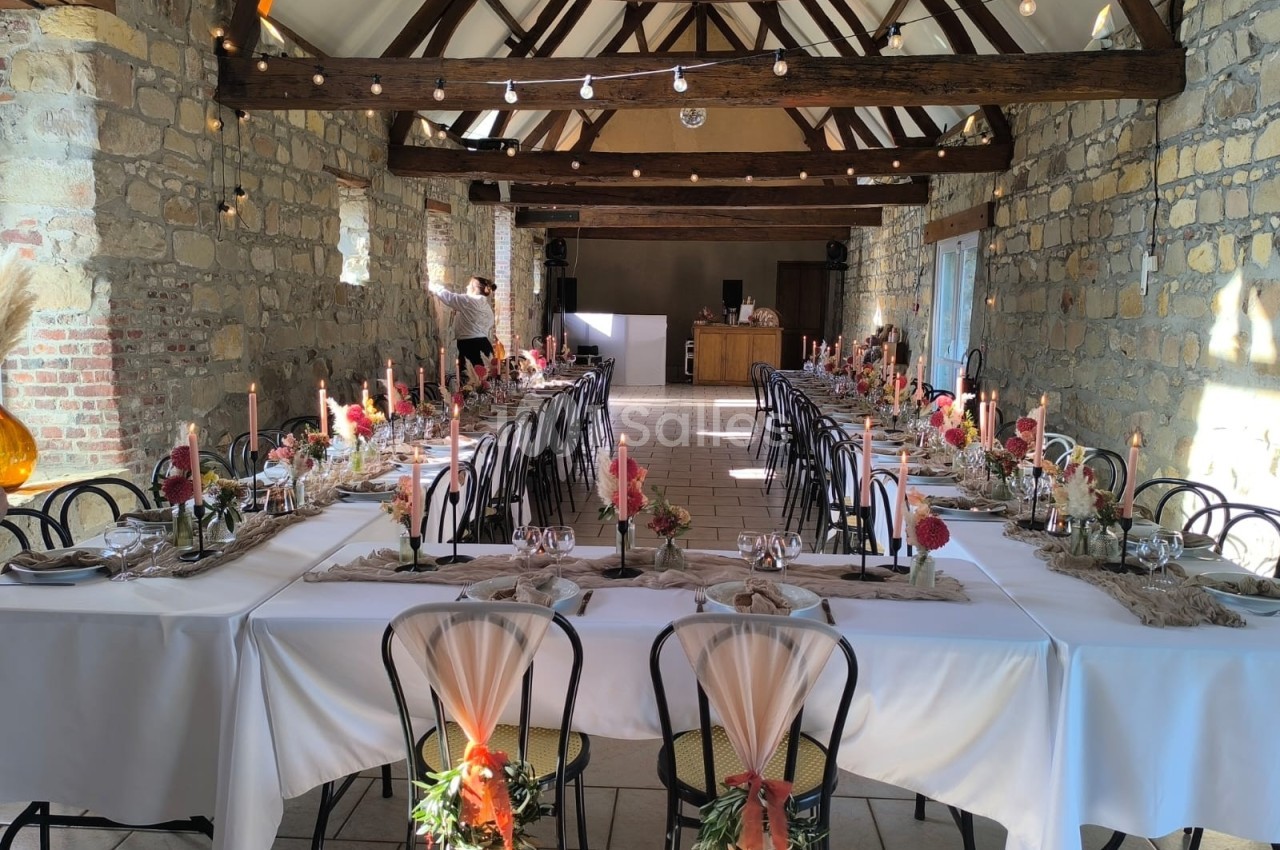Salle de réception en pierre avec tables dressées, décorations florales et bougies, éclairée par la lumière naturelle.