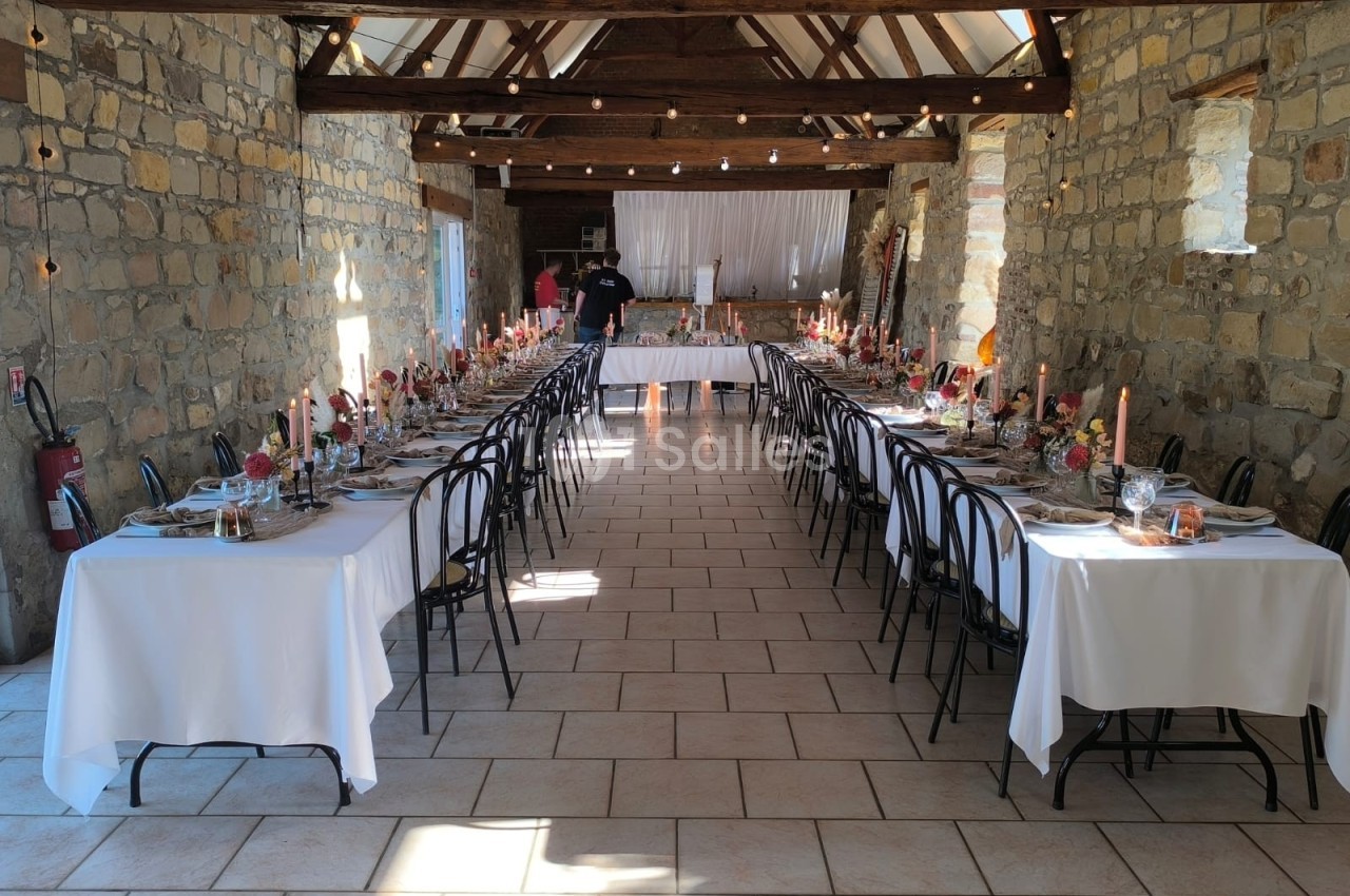 Salle en pierre aménagée pour un banquet, avec longues tables dressées, bougies et décorations florales.