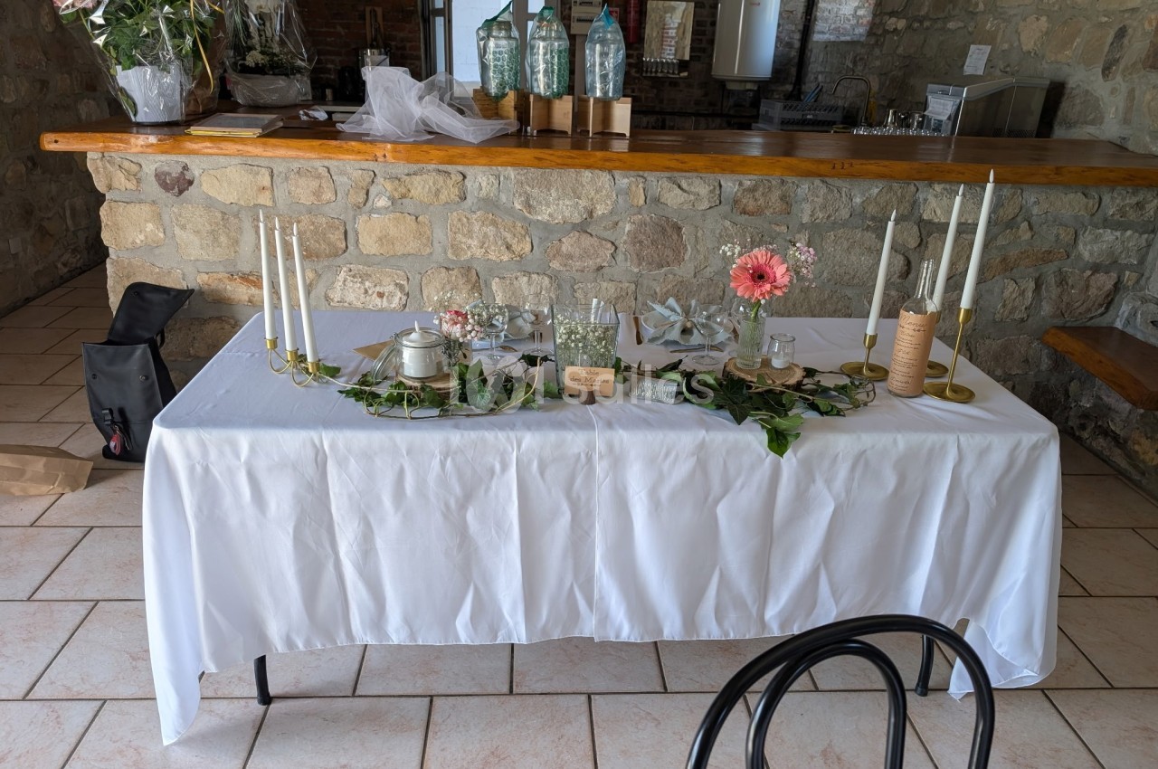 Table décorée avec nappe blanche, bougies, fleurs et éléments végétaux dans un intérieur en pierre.