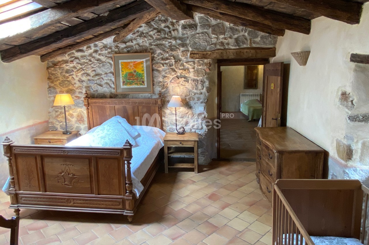 Chambre rustique avec lit en bois sculpté, murs en pierre, poutres apparentes et mobilier en bois.