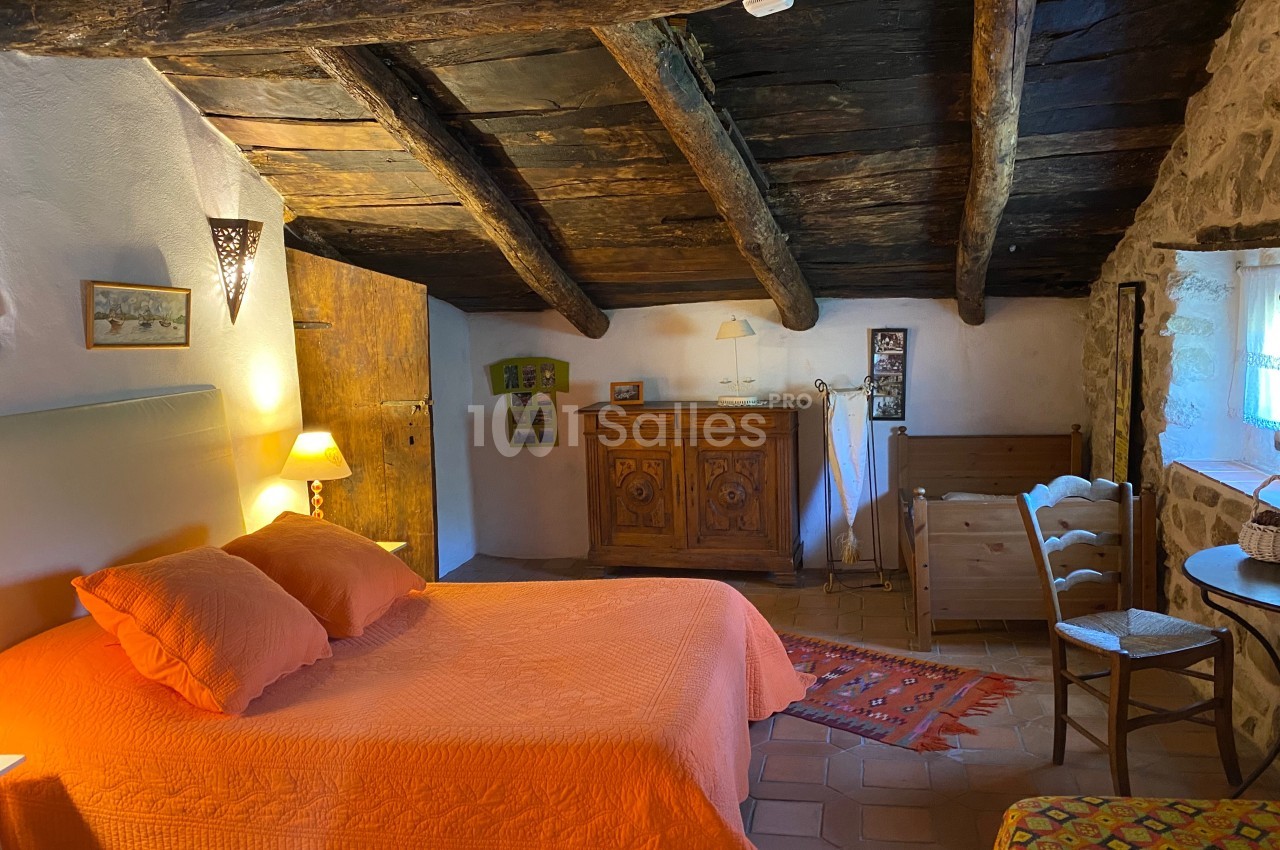 Chambre rustique avec poutres apparentes, lit double orange, mobilier en bois et lumière douce.
