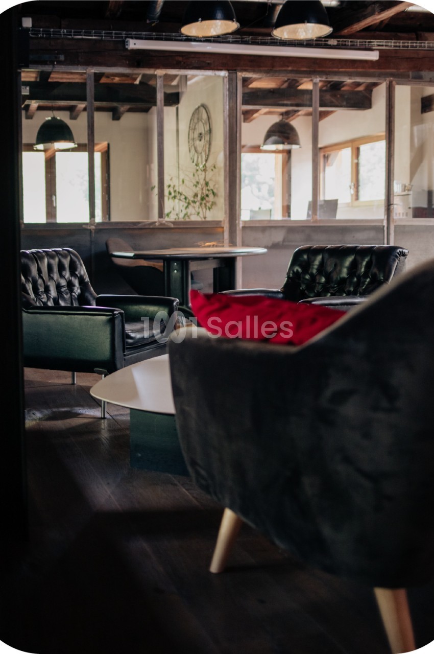 Espace intérieur avec fauteuils en cuir, table basse et grandes fenêtres laissant entrer la lumière naturelle.