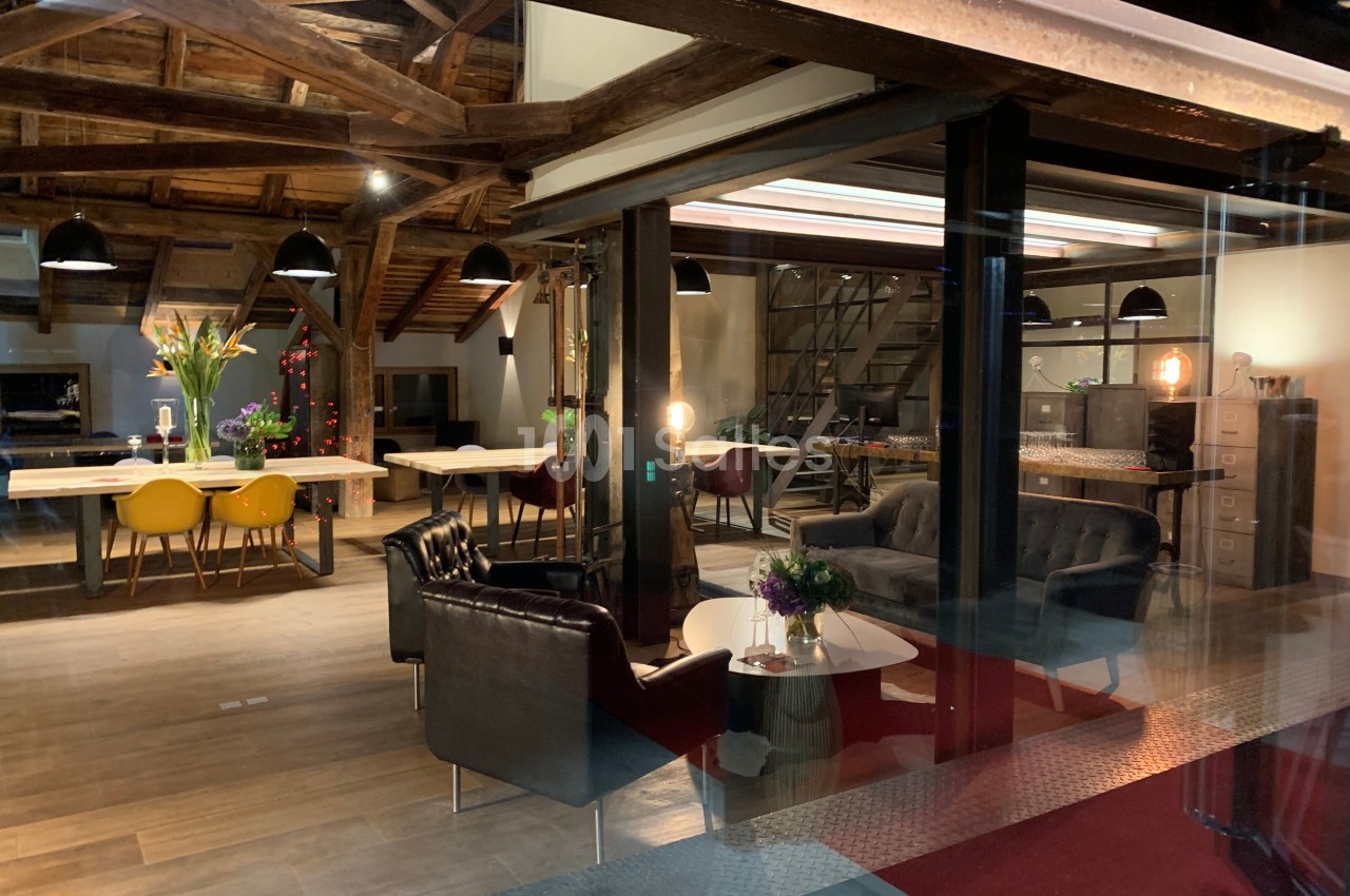 Espace intérieur moderne et chaleureux avec poutres apparentes, mobilier design et éclairage tamisé.