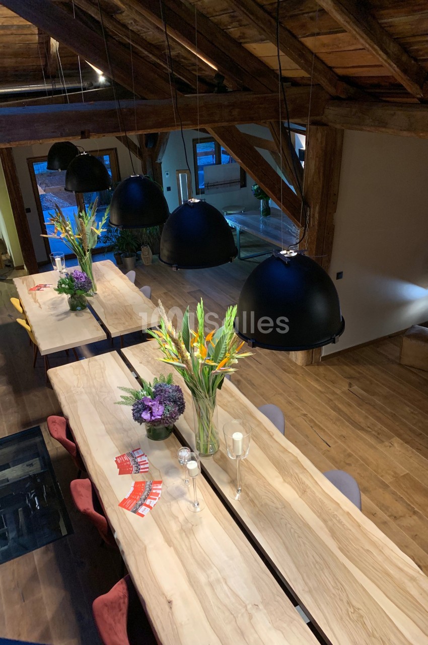 Salle à manger avec de longues tables en bois, décorées de bouquets de fleurs et éclairées par des suspensions noires.