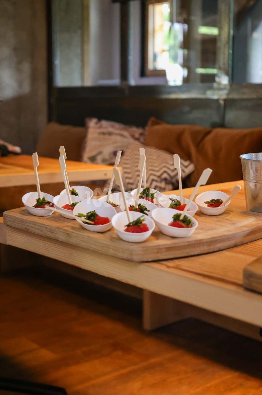 Petites portions de nourriture servies dans des coupelles blanches avec des piques, disposées sur une planche en bois.